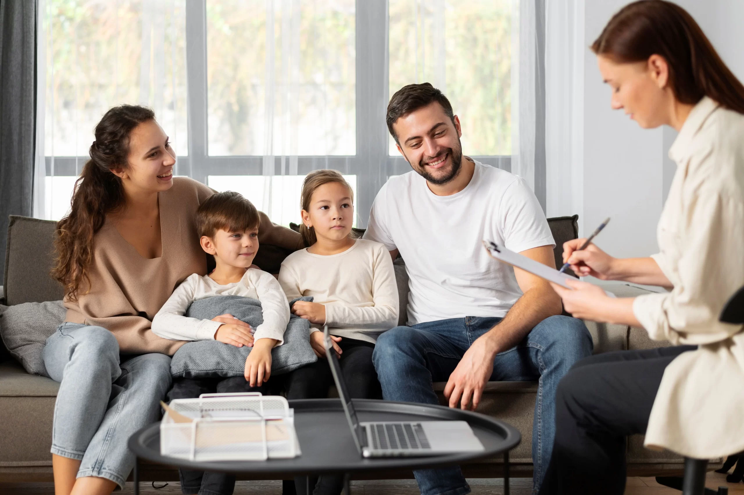 A family of four sitting on a couch, looking at a laptop screen together. or a family registered themselves for a family sponsorship Canada,